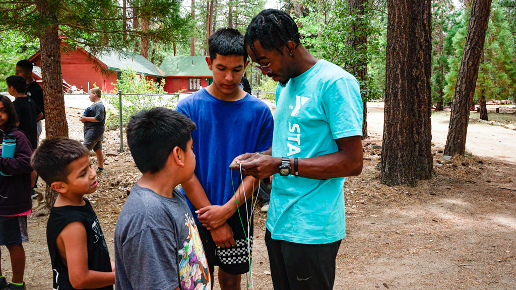 Camp Edwards counselor teaching children to make a lanyard