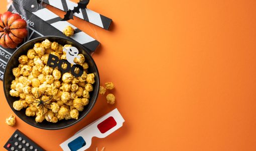 Halloween-themed setup with popcorn, movie clapperboard, pumpkin, and spooky decorations on an orange background